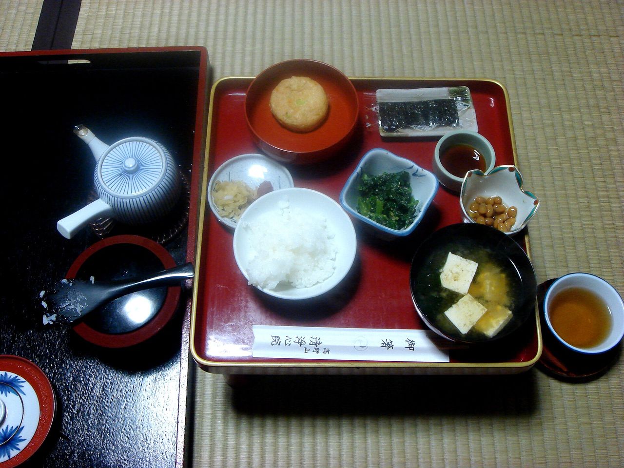 ご飯、豆腐の味噌汁、納豆、漬物、お茶が膳に並ぶ寺院の朝食