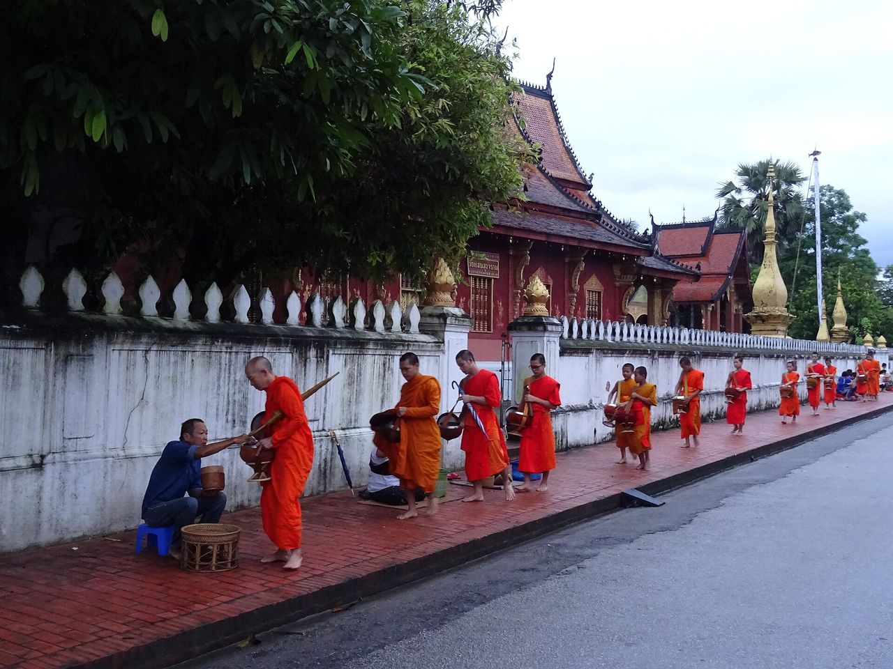 A distant view of monks walking in a line along a temple wall during the alms-giving ceremony
