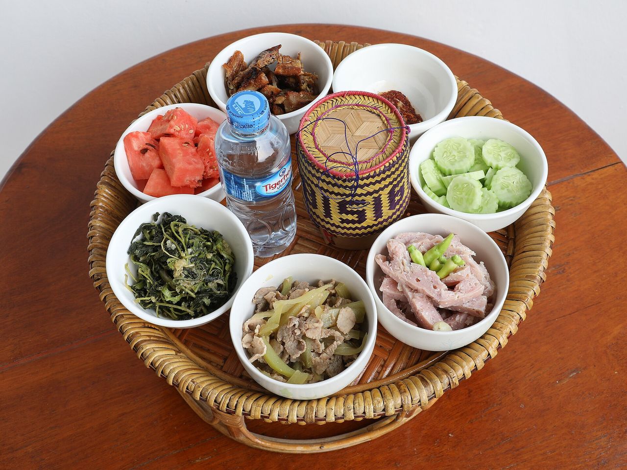 もち米の小さな籠を中心に、野菜、果物、豚肉や鶏肉の料理を盛った盆