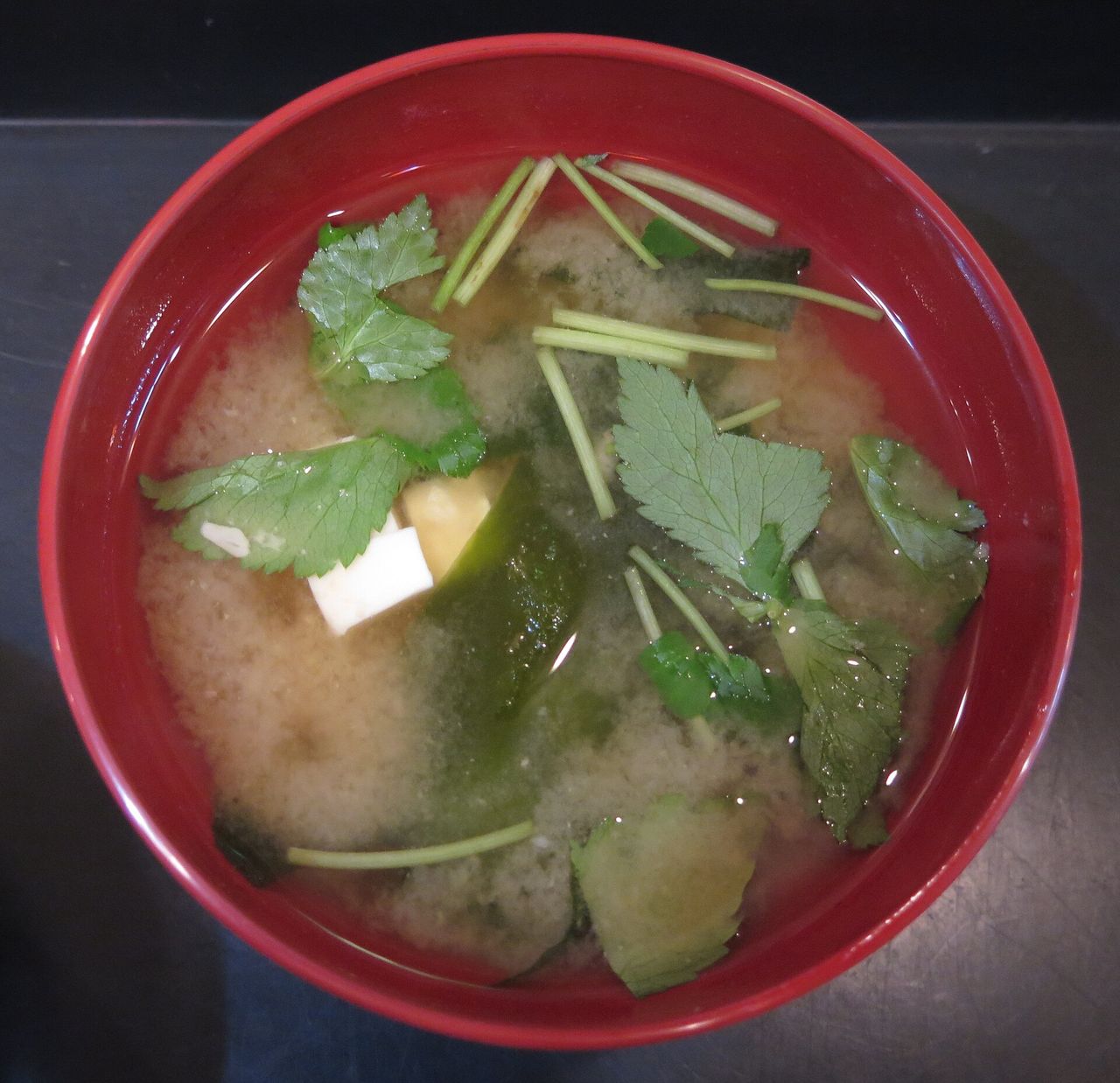 豆腐と海藻が入った赤い椀のみそ汁を真上から見た写真